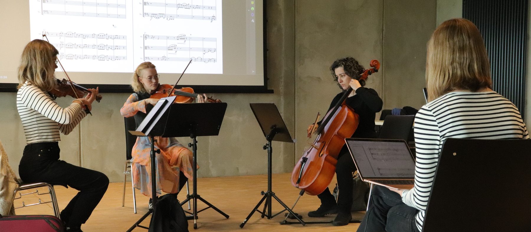 The string trio playing a participant’s piece, the score projected behind them